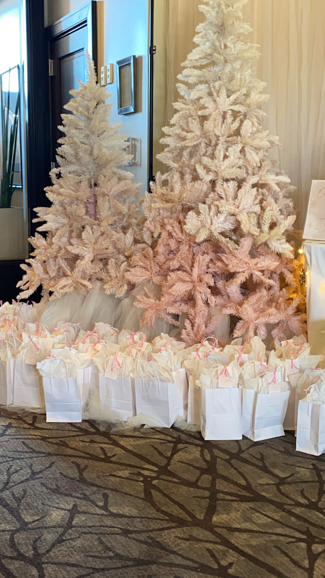 Blush and ivory holiday trees styled with tulle and coordinated guest gifting at a hospitality entrance
