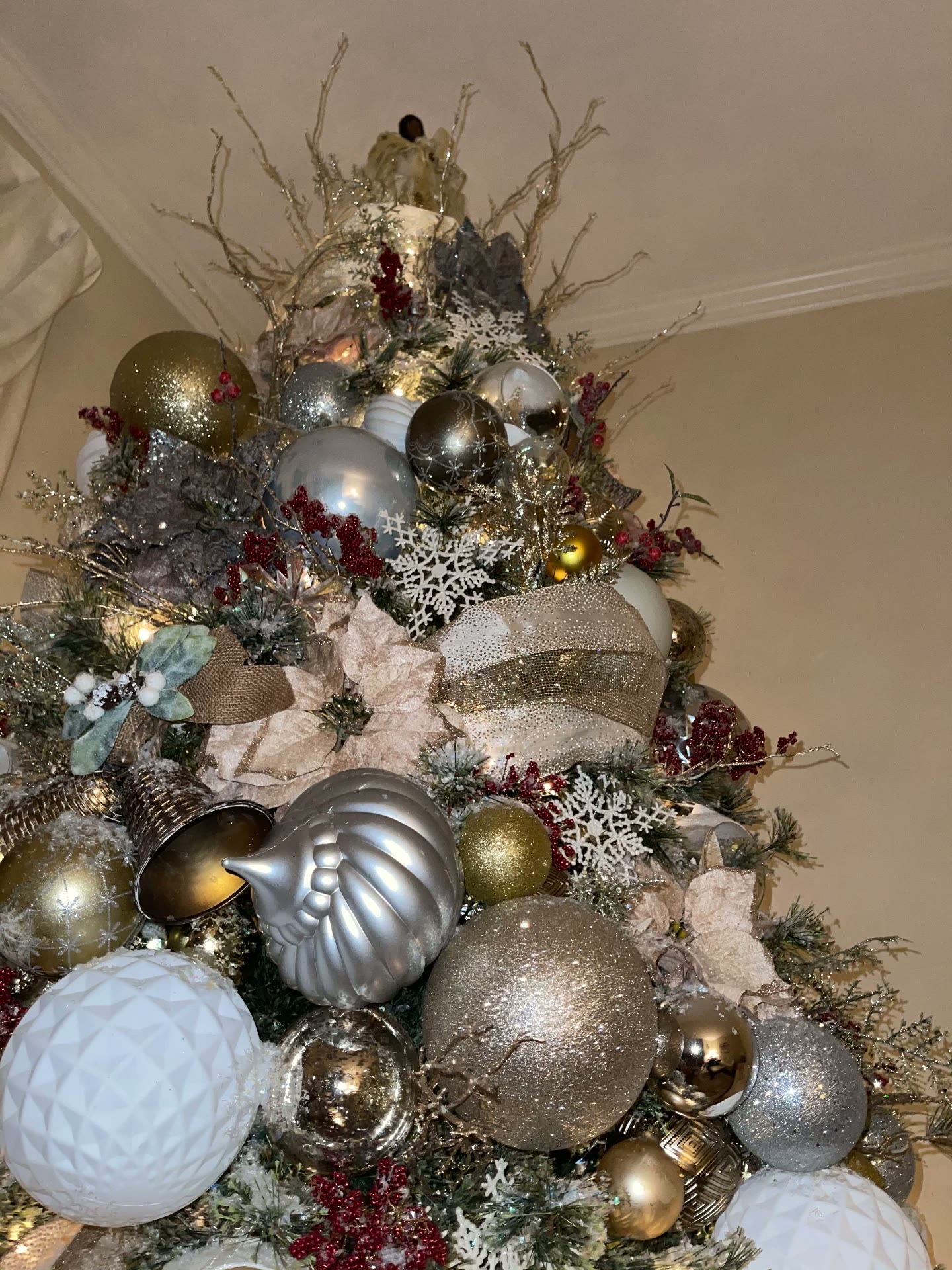 Close detail of layered ornaments, oversized baubles, ribbon, florals, berries, and warm lighting on a designer holiday tree